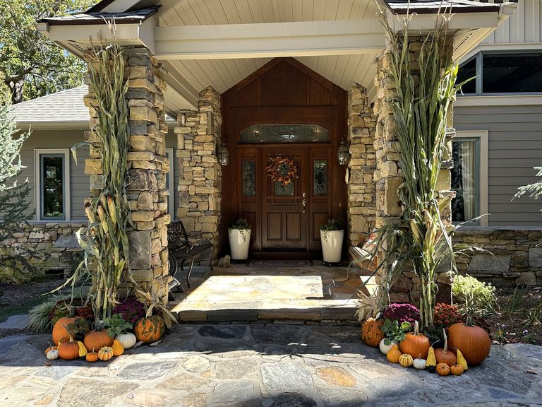 Harvest entry styled with pumpkins, gourds, and mums beside a stone porch