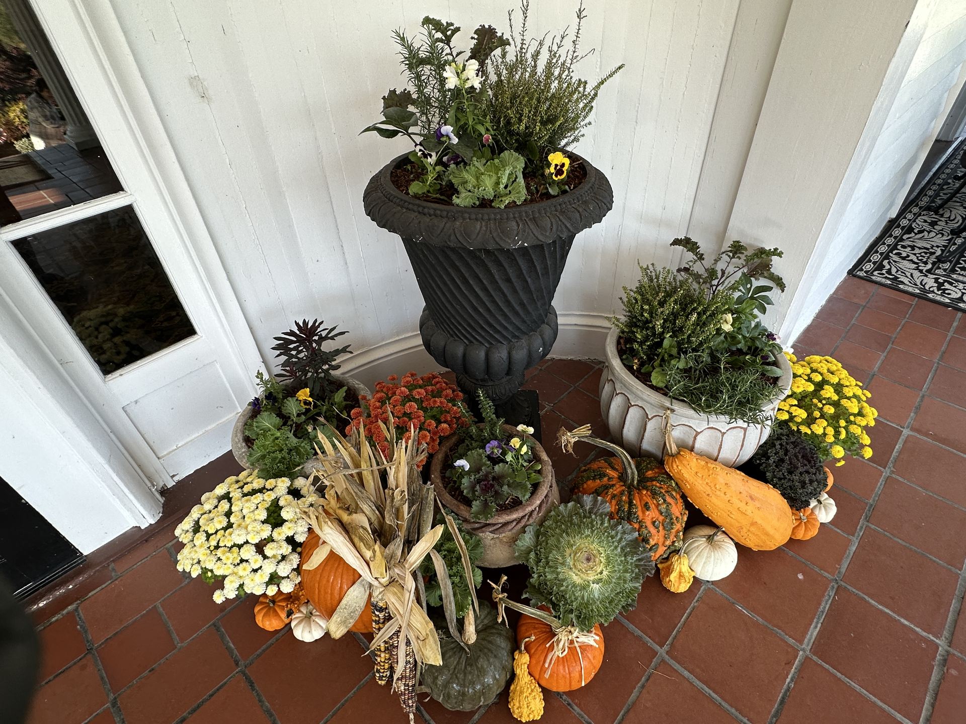 Fall entrance styled with cool-season planters, ornamental cabbage, mums, pumpkins, gourds, and corn