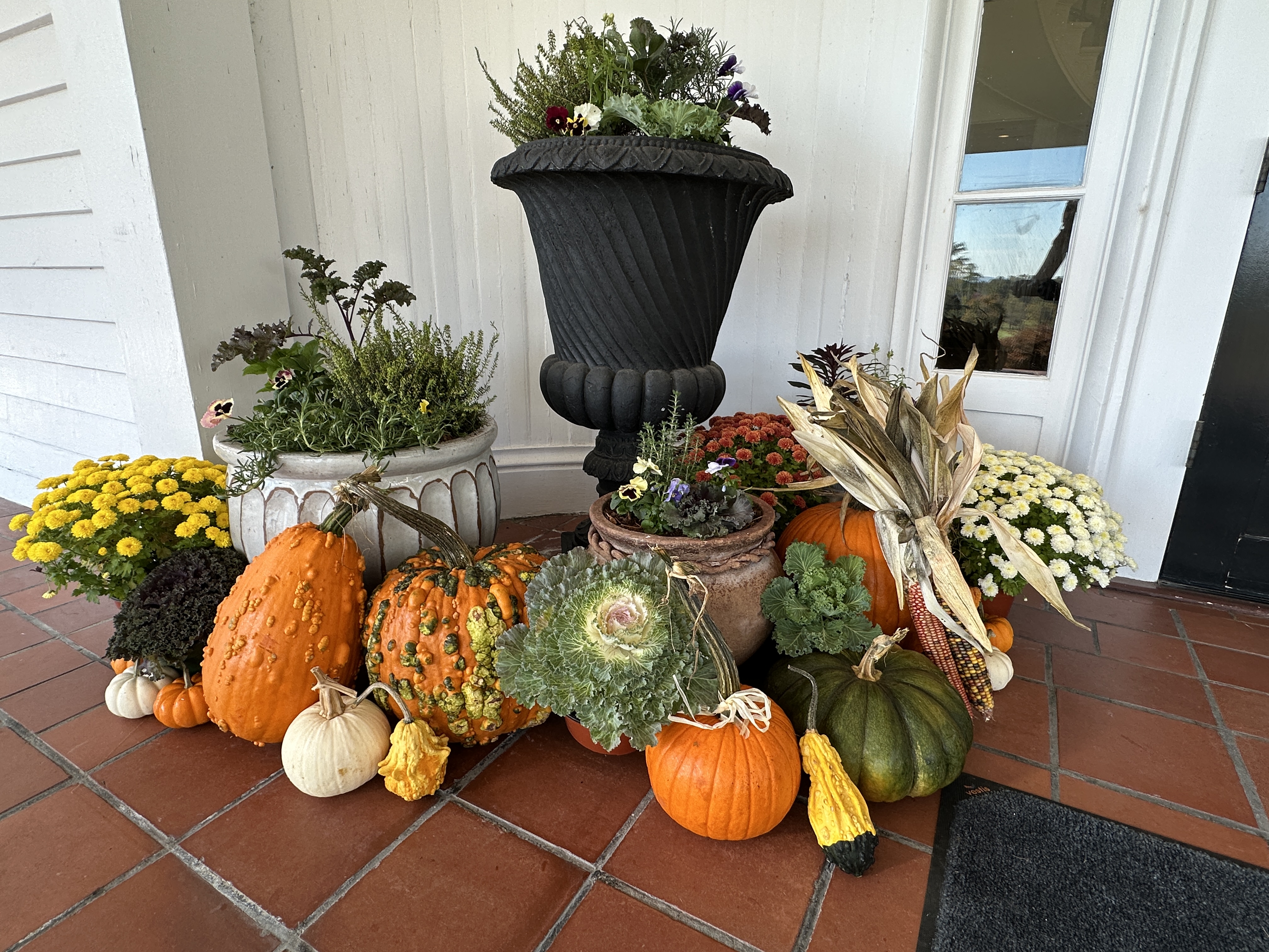 Layered fall porch with corn stalks, gourds, and seasonal planters